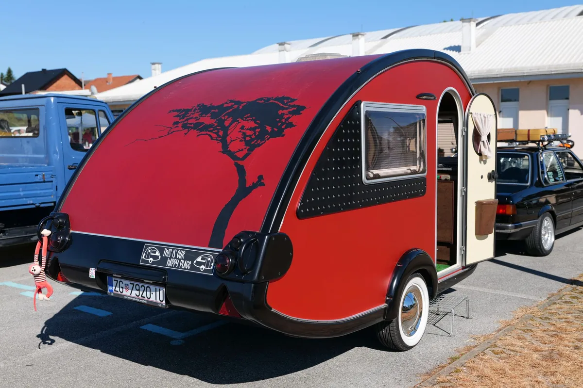 A compact red-and-silver teardrop camper trailer hitched for towing