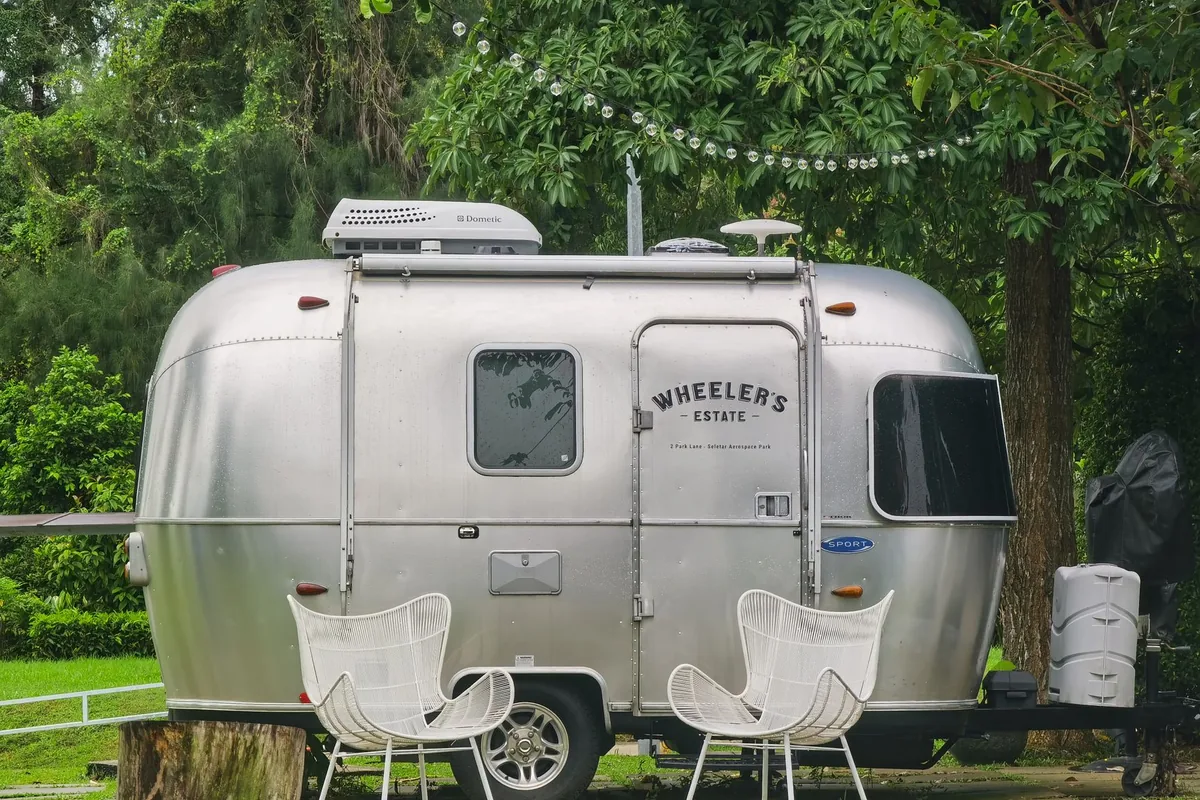 A polished silver travel trailer with chairs set out on the grass