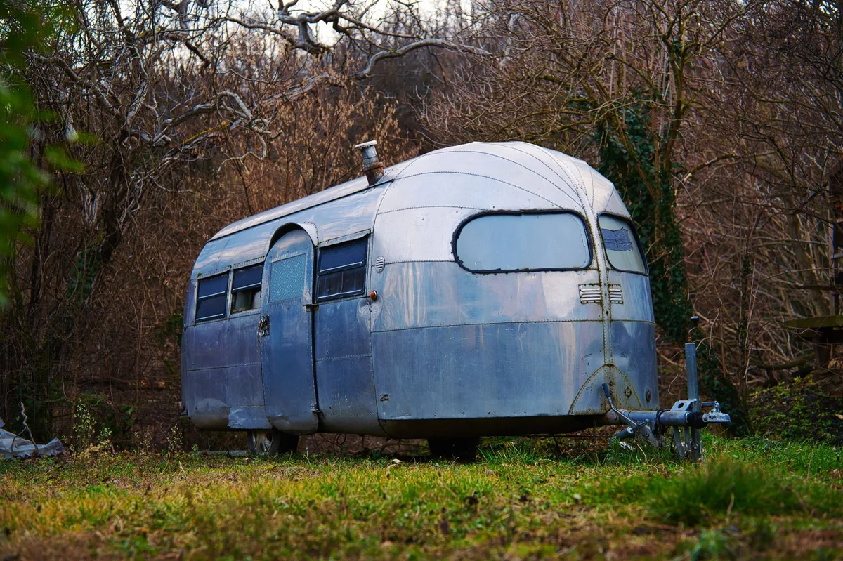 A vintage silver riveted travel trailer parked among greenery