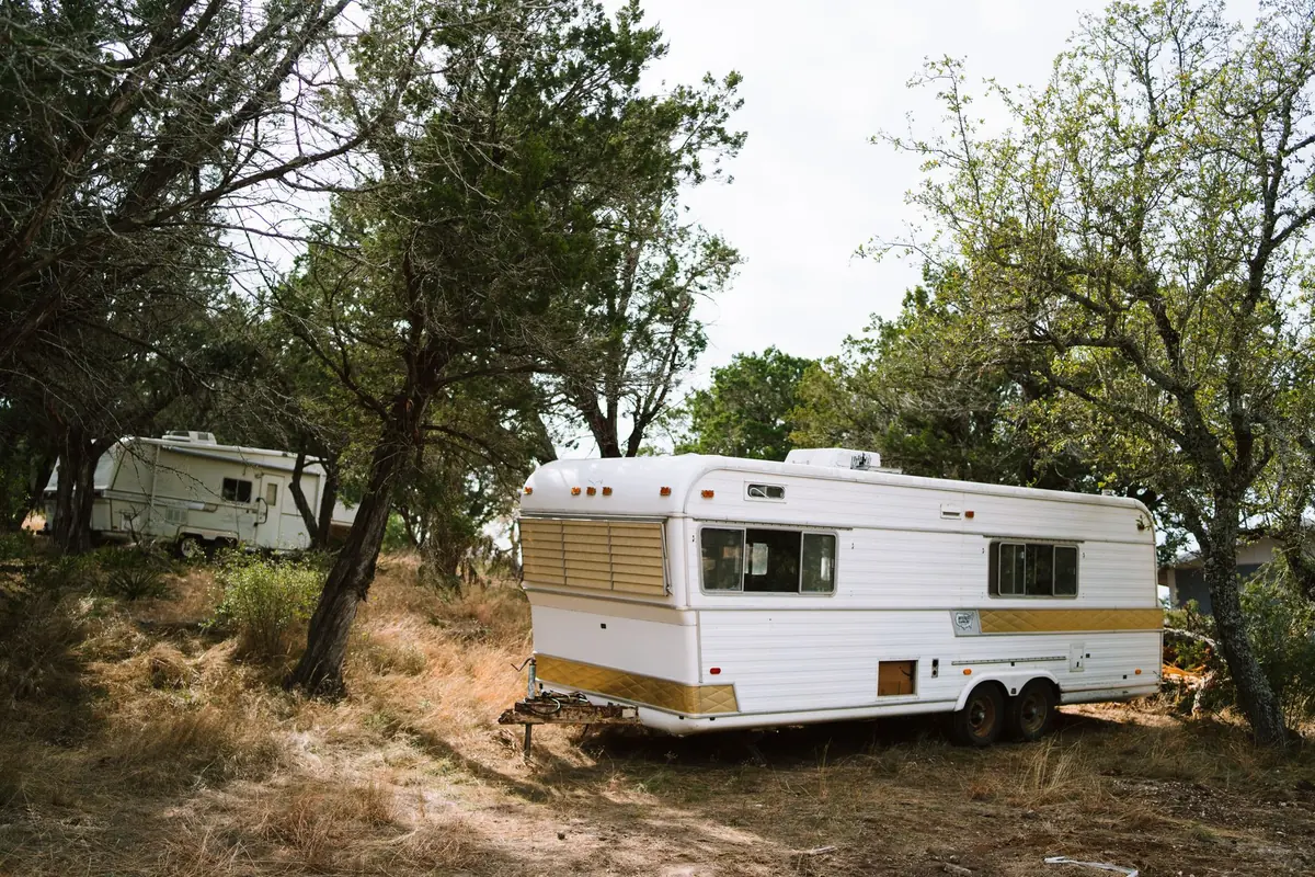 A white travel trailer parked among trees at a wooded campsite