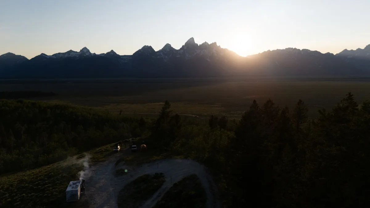 An RV silhouetted against the sun setting behind a mountain range