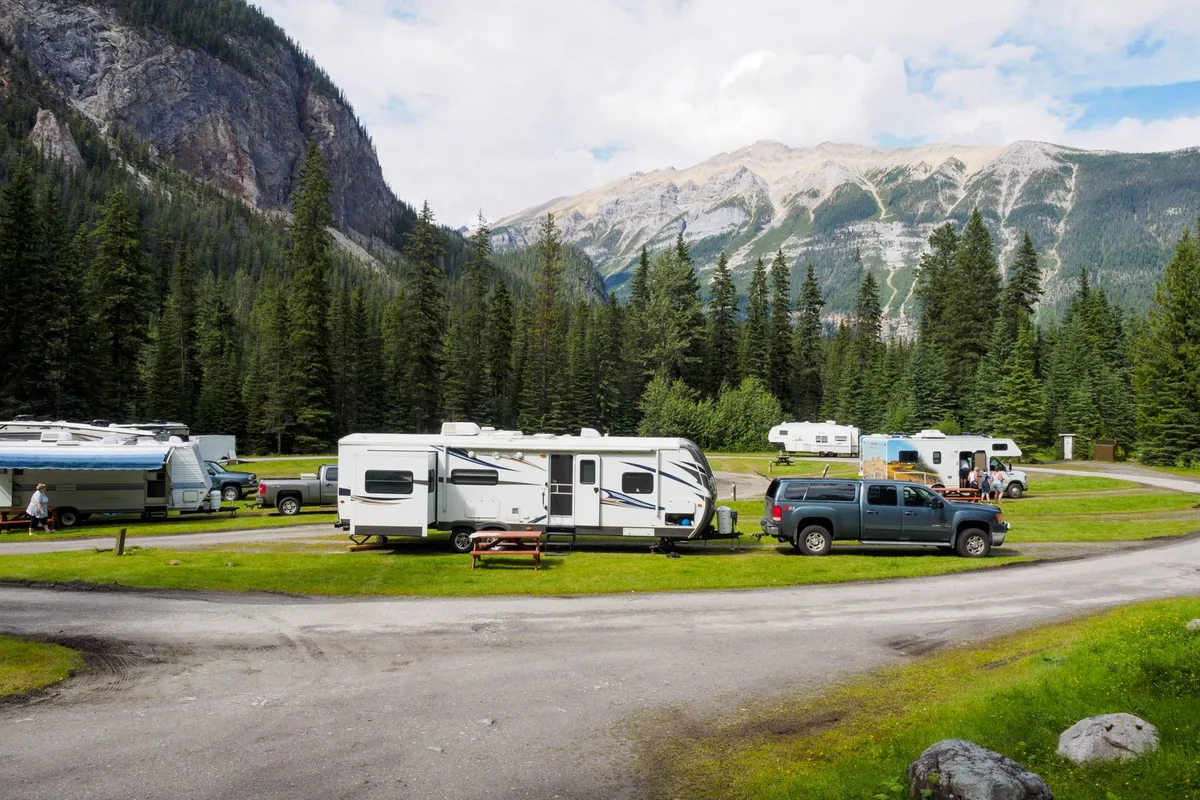 A row of travel trailers at a campground beneath forested mountains