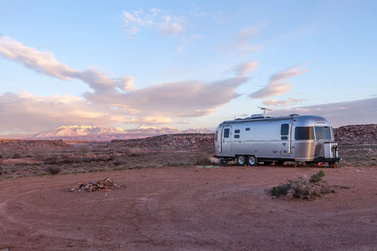 A silver travel trailer parked in open desert under a wide evening sky