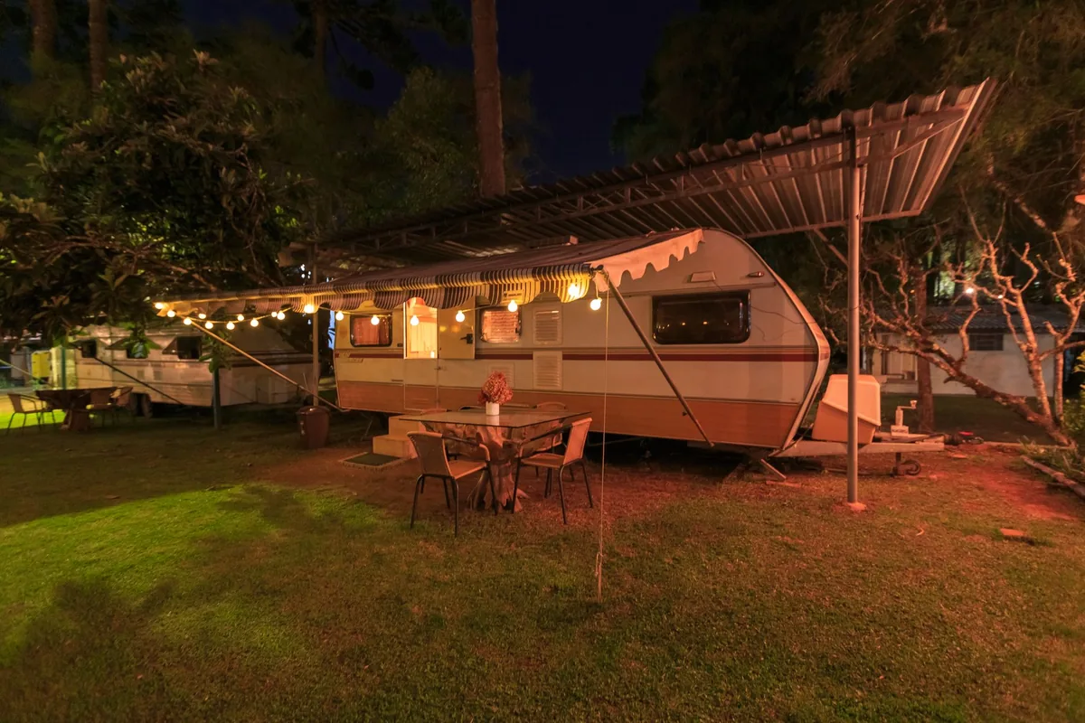 A travel trailer lit with string lights at a grassy campsite in the evening